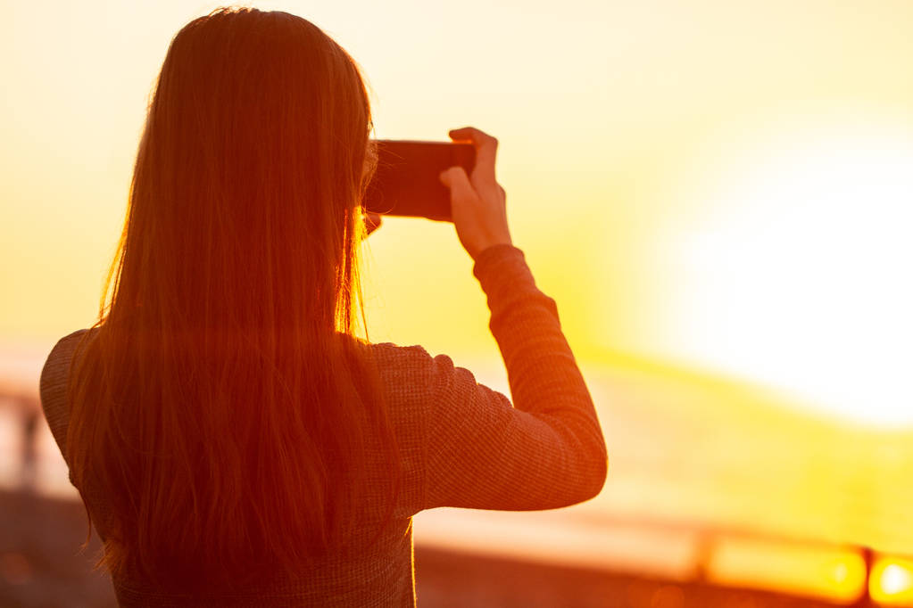 Młoda kobieta fotografie zachód słońca na plaży.  - Zdjęcie, obraz