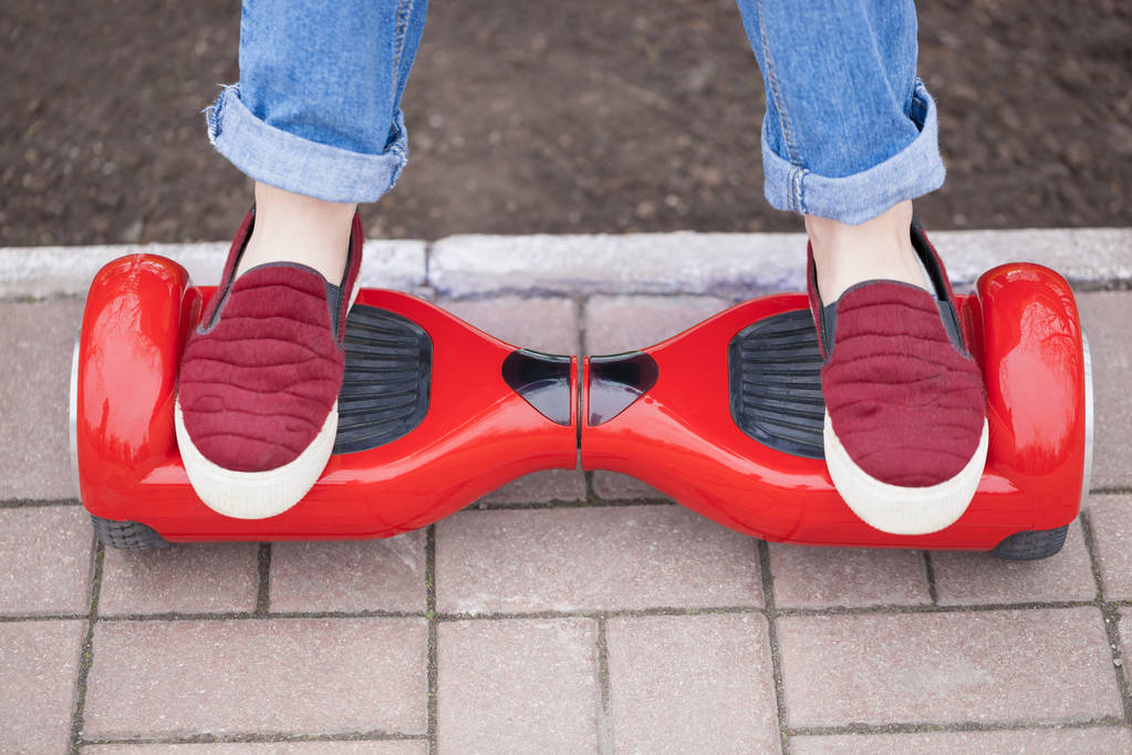 Pies de gir en zapatos marsala montados en un moderno mini segway eléctrico rojo o un scooter de tabla flotante. Tendencia nueva tecnología de transporte que es tan divertido y fácil de montar y no produce contaminación del aire a la atmósfera. Concéntrate en el dispositivo
 - Foto, Imagen