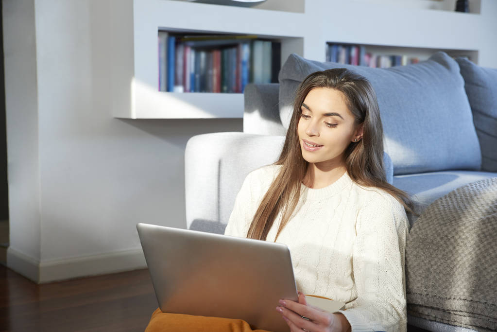 Portrét krásné mladé ženy používající její laptop sedí na gauči doma. Domácí kancelář. - Fotografie, Obrázek