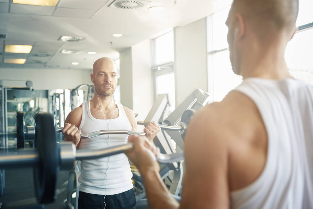 Primer plano del hombre en el gimnasio haciendo ejercicios de mancuerna para crear el cuerpo más muscular
. - Foto, imagen