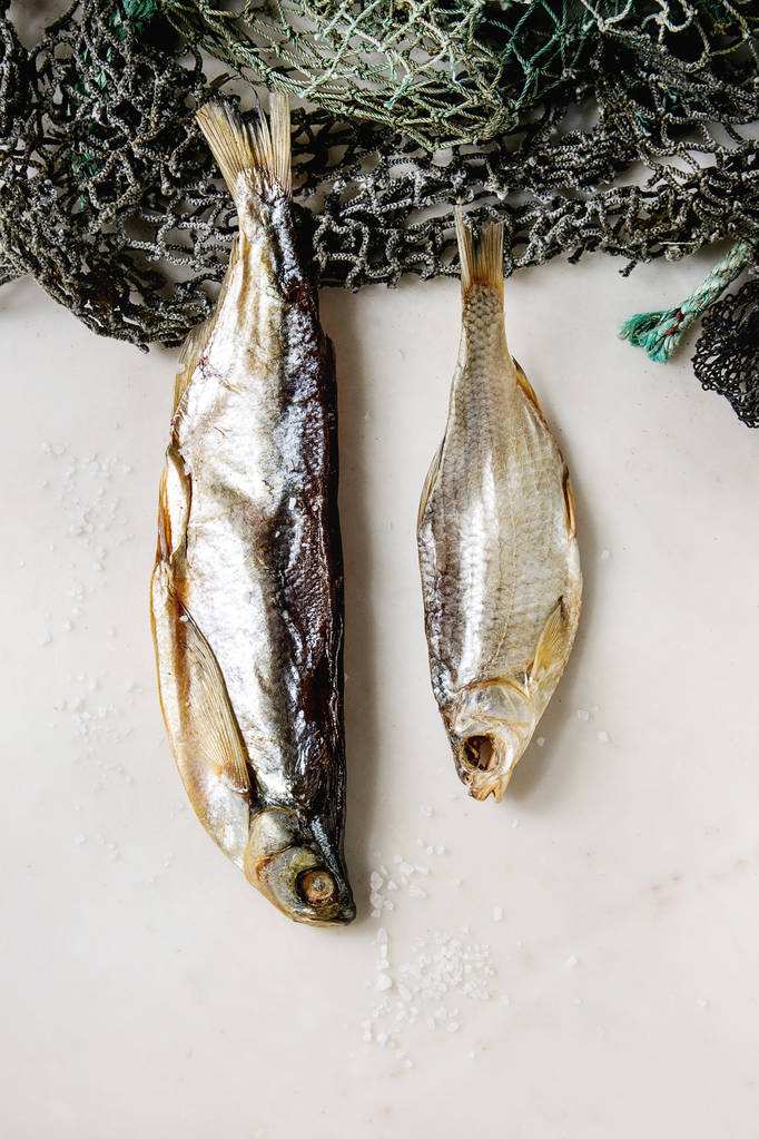 Gedroogde vis of stockfish op visnetten over witte marmeren achtergrond. Platte lay, ruimte - Foto, afbeelding