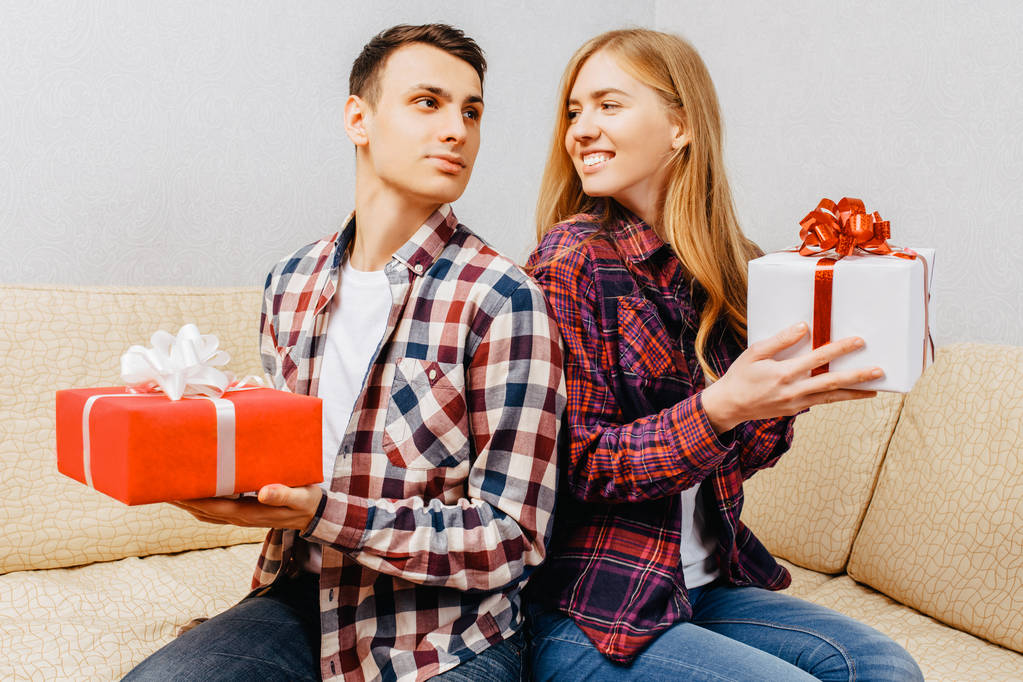 pareja joven, hombre y mujer se dan regalos mientras están sentados en casa en el sofá
 - Foto, imagen