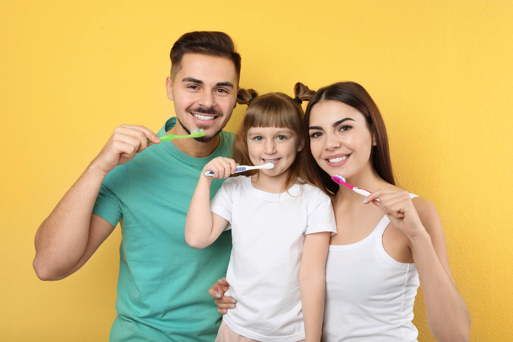 kleines Mädchen und ihre Eltern beim gemeinsamen Zähneputzen auf farbigem Hintergrund - Foto, Bild
