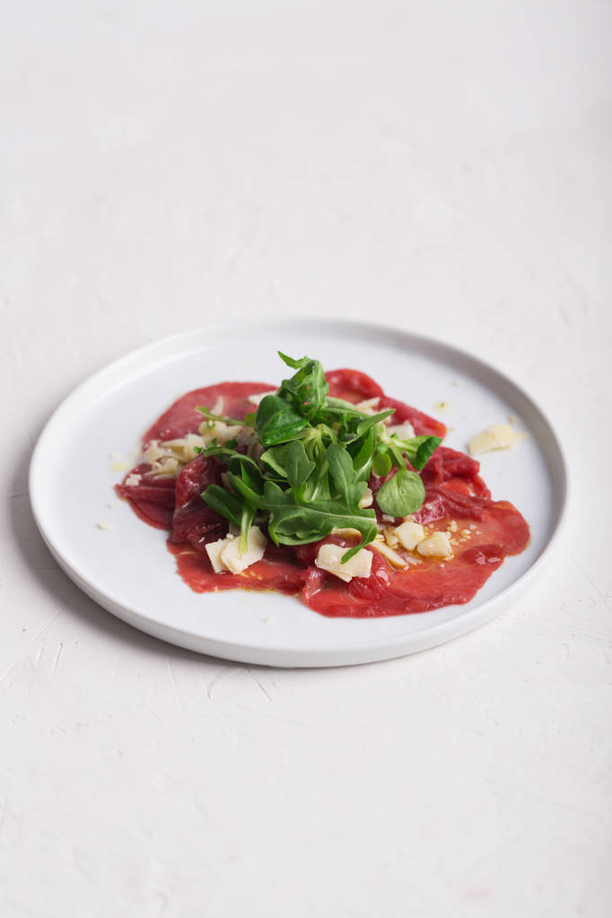 Rundercarpaccio met rucola salade, Parmezaanse kaas en saus op de witte plaat - Foto, afbeelding