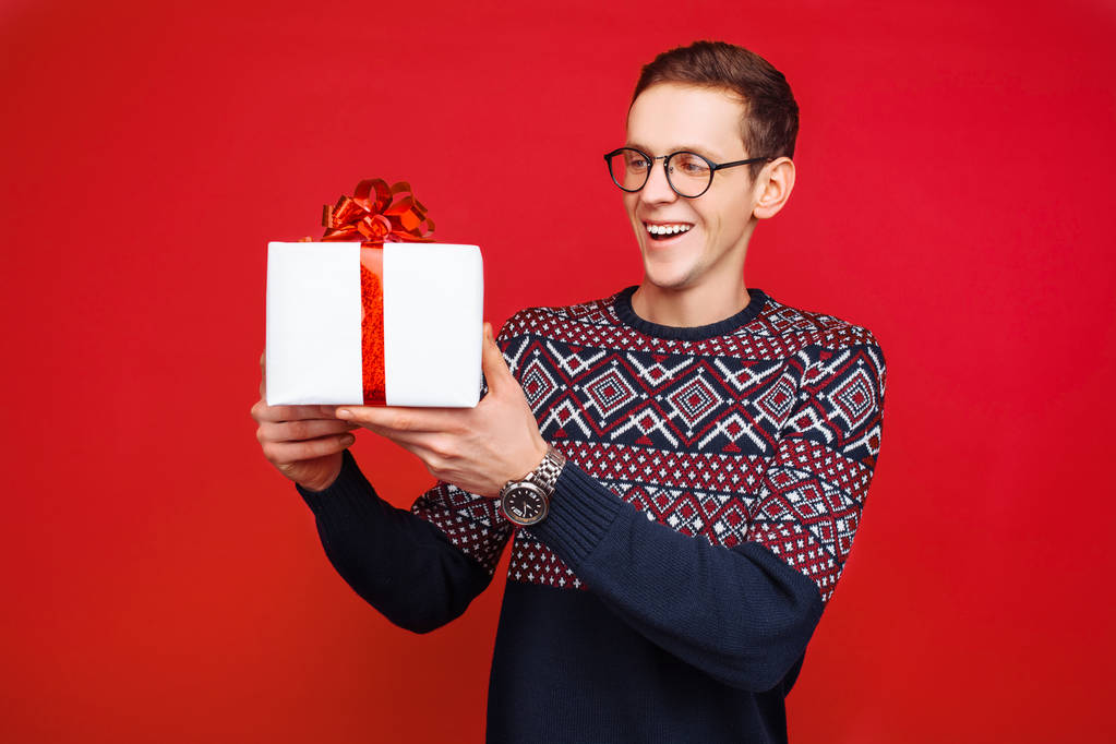 Portret van een man met bril, met een gift box in de hand, op een rode achtergrond - Foto, afbeelding