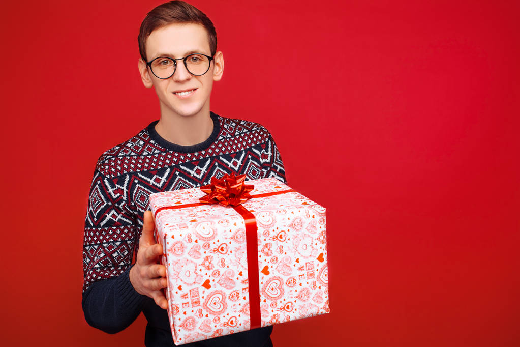 Hombre en gafas con una caja de regalo en las manos sobre un fondo rojo
 - Foto, Imagen