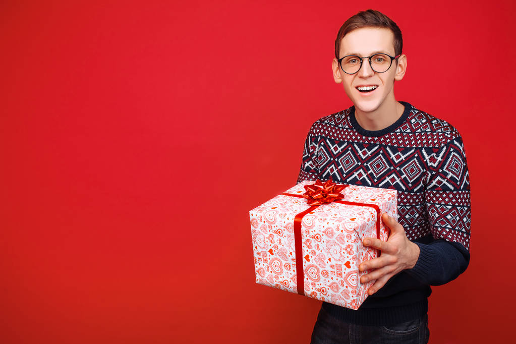 Gözlüklü adamla kırmızı bir arka plan üzerinde elinde bir hediye kutusu - Fotoğraf, Görsel