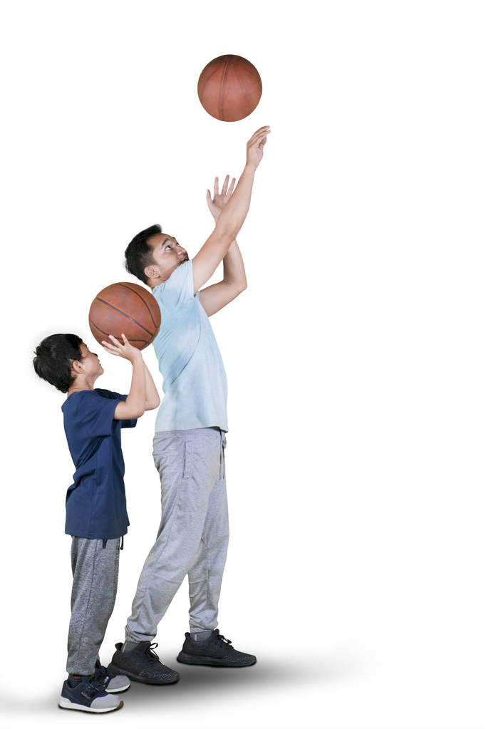 Young man teaching his son to shooting a basketball while exercising in the studio - Photo, Image