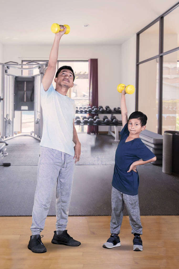 Portrait de heureux petit garçon et son père soulevant un haltère tout en exerçant ensemble dans le centre de gymnastique
 - Photo, image
