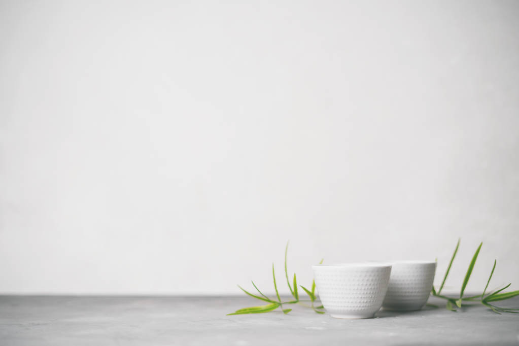 conjunto con tazas de té de porcelana blanca con hojas de bambú verde sobre fondo gris claro
 - Foto, imagen