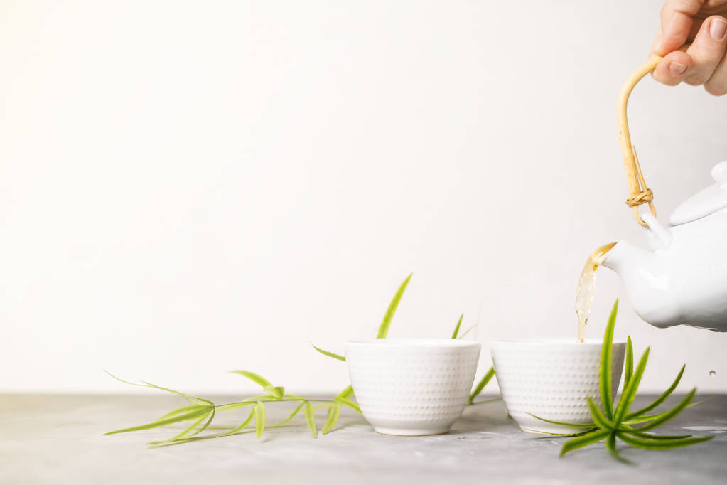 Mano femminile versando il tè verde da una teiera in tazze su sfondo bianco con spazio copia. Set da tè asiatico
.  - Foto, immagini