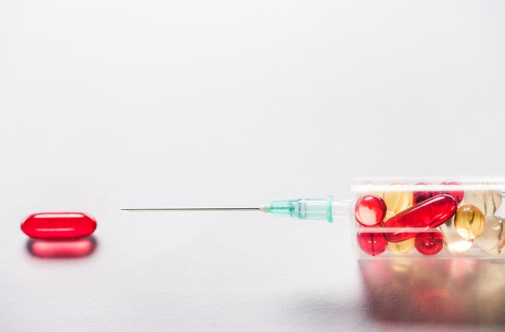 灰色の背景の赤い楕円形錠剤近く薬で注射器のクローズ アップ  - 写真・画像