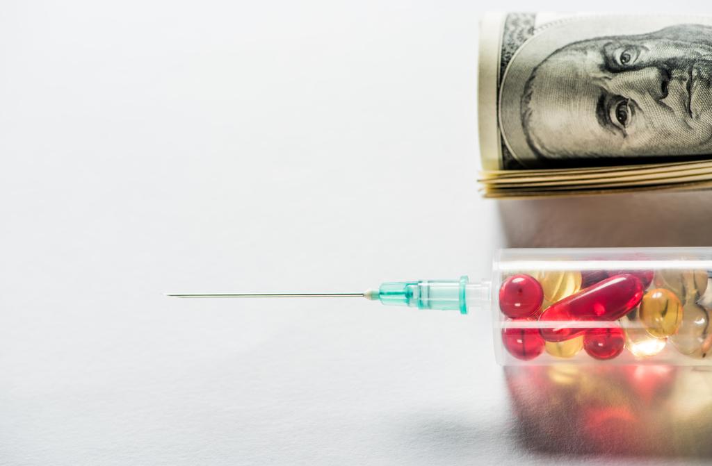 primer plano de la jeringa con medicamentos cerca de rollo de dinero sobre fondo gris
  - Foto, Imagen