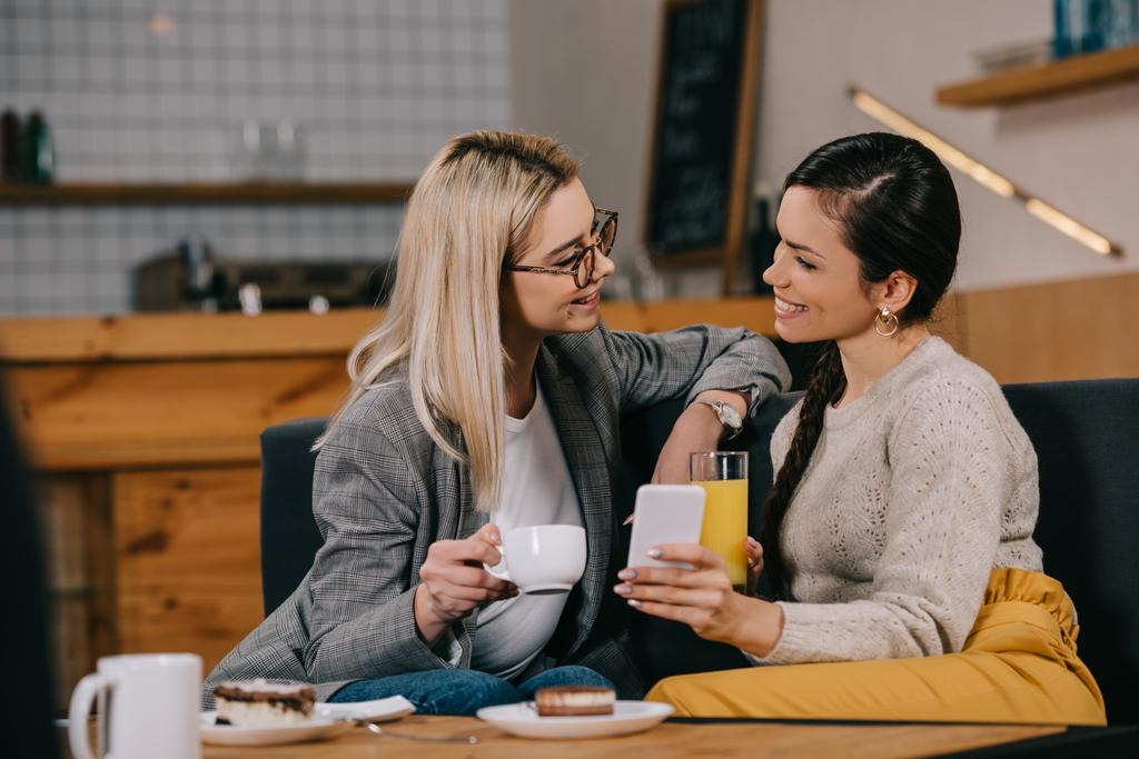 glimlachende vrouwen chatten terwijl dranken in café - Foto, afbeelding