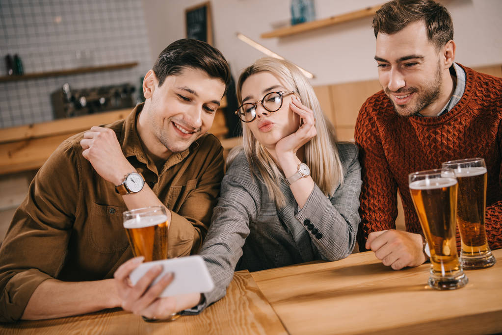 привлекательная женщина делает селфи с друзьями-мужчинами возле бокалов пива
 - Фото, изображение