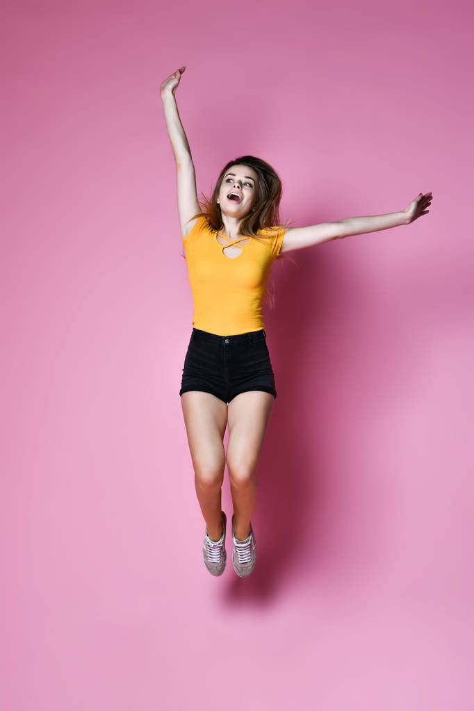 Porträt eines fröhlichen positiven Mädchens, das in die Luft springt und die Kamera isoliert auf rosa Hintergrund betrachtet. - Foto, Bild