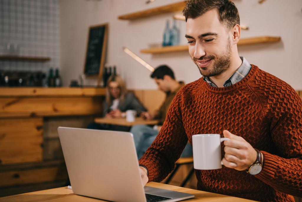 vidám ember látszó-on laptop-miközben kávét a café - Fotó, kép