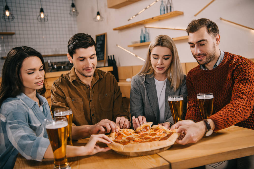 group of friends smiling while taking pieces of tasty pizza in bar - Photo, Image