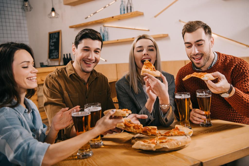 Gelukkige vrouw eten van pizza in de buurt van vrienden in staaf - Foto, afbeelding