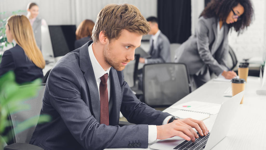 geconcentreerde jonge zakenman laptop gebruikt terwijl u werkt in een open ruimte kantoor  - Foto, afbeelding