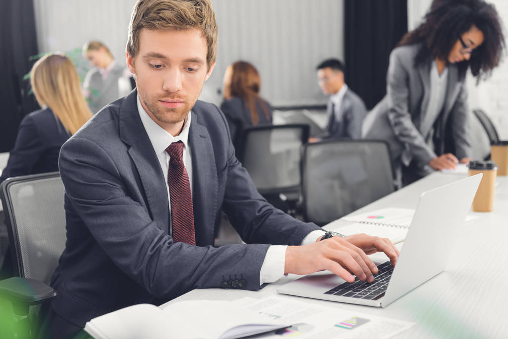 серьезный молодой бизнесмен смотрит на ноутбук и с помощью ноутбука в офисе
  - Фото, изображение