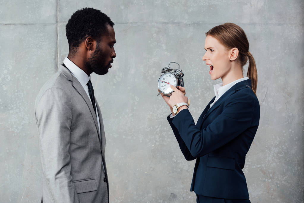 афро-американських бізнесмен, дивлячись на кричали підприємець, вказуючи на годинник на сірий фон - Фото, зображення