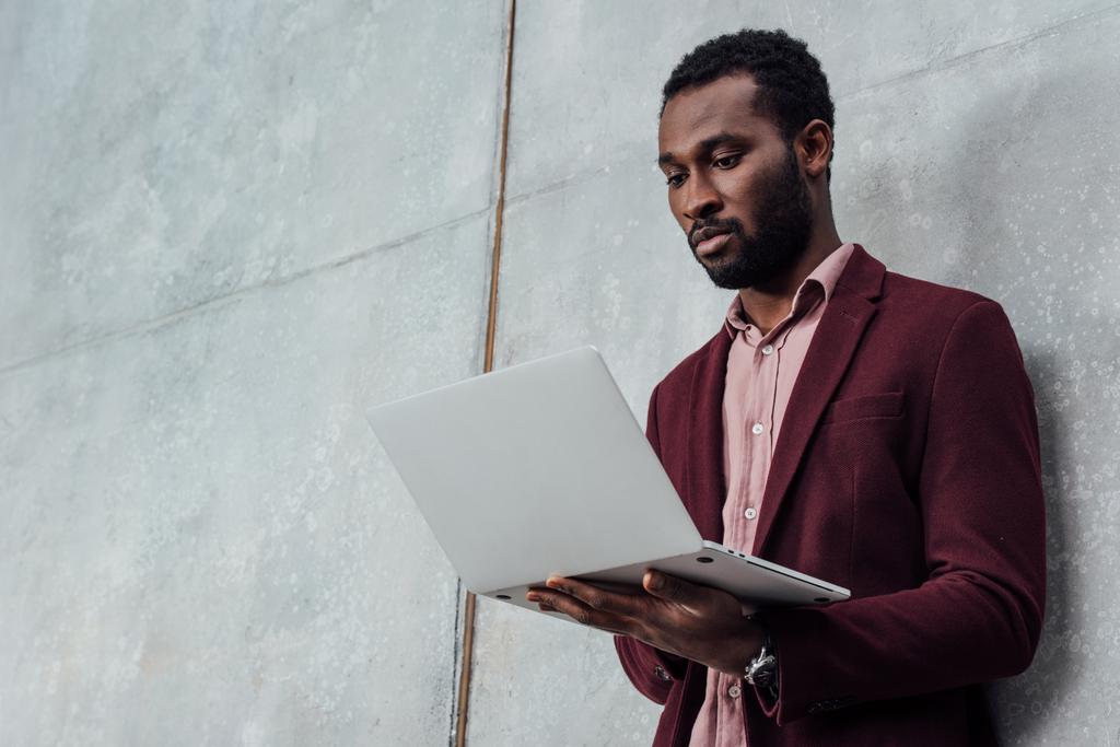 hombre de negocios ocasional afroamericano serio usando el ordenador portátil sobre fondo gris
 - Foto, imagen