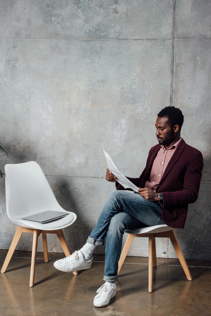 Afrikkalainen amerikkalainen rento liikemies istuu ja lukee sanomalehteä odotussalissa
 - Valokuva, kuva