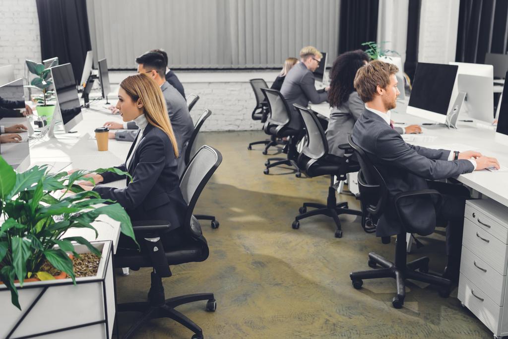 Zijaanzicht van professionele jonge ondernemers in formele slijtage werken met desktopcomputers in kantoor - Foto, afbeelding