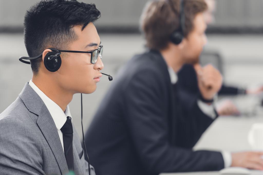 widok boczny skupia młodych azjatycki biznes biznesmen w zestaw słuchawkowy działa z kolegami w biurze - Zdjęcie, obraz