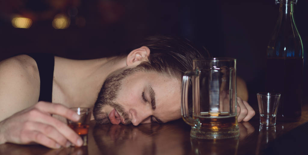 Alcohol abuse. Man sleep after drinking strong alcoholic beverage and beer in pub. Alcoholic man sleeping at bar counter. Alcohol addict with alcohol drink. Alcohol addiction and bad habit - Photo, Image
