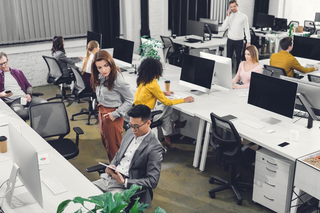 hoge hoekmening van jonge multi-etnische ondernemers werken met digitale apparaten in open ruimte kantoor - Foto, afbeelding