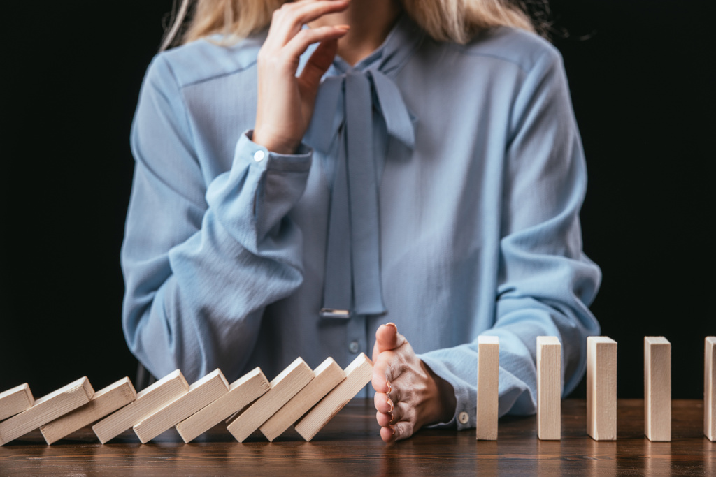 cropped view of woman in blue blouse sitting at desk and preventing wooden blocks from falling with hand - Photo, Image