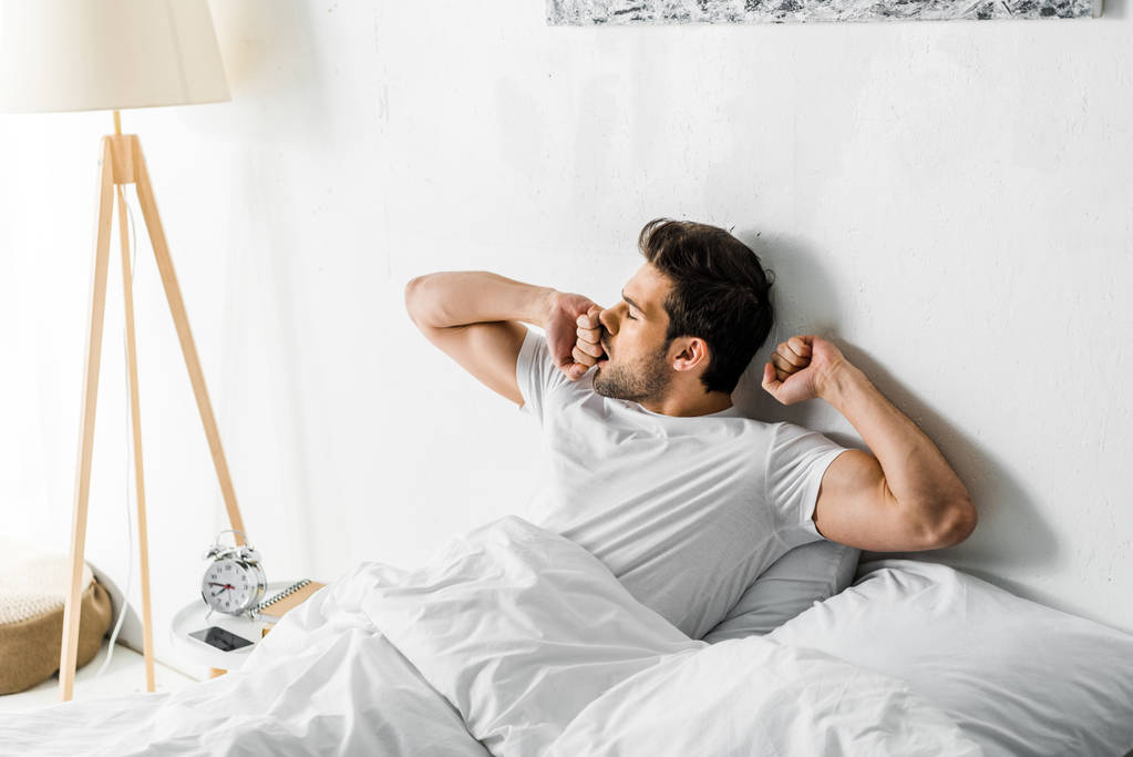 Красивый мужчина зевает и просыпается в постели утром
 - Фото, изображение