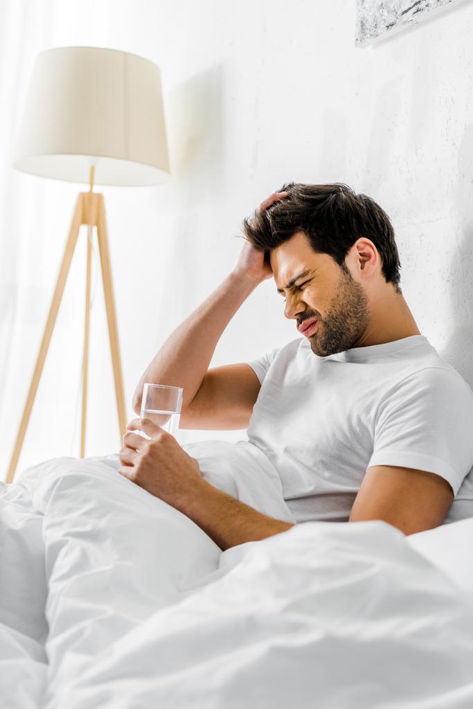 hombre cansado con resaca sosteniendo un vaso de agua en la cama por la mañana
 - Foto, imagen