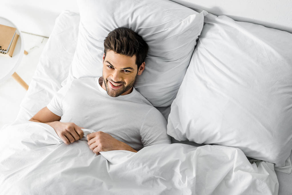 ylhäältä näkymä komea iloinen mies makaa sängyssä aamulla
 - Valokuva, kuva