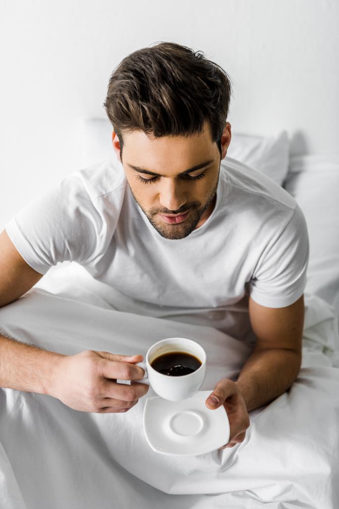 bel homme souriant en pyjama tenant une tasse de café au lit
 - Photo, image