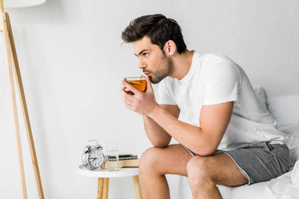 Красивый мужчина в пижаме пьет чай в спальне
 - Фото, изображение