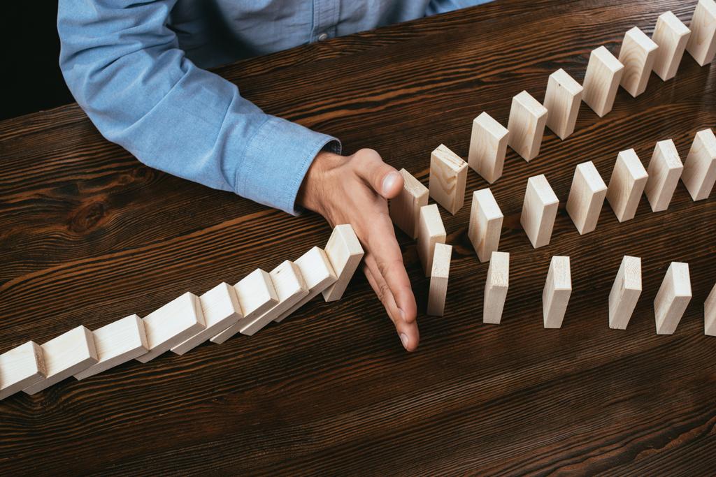 cropped view of man at desk preventing wooden blocks from falling  - Photo, Image