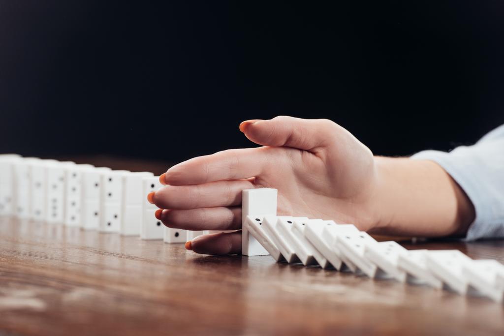 vista recortada de la mujer evitando que los dominós caigan en el escritorio aislado en negro
 - Foto, imagen