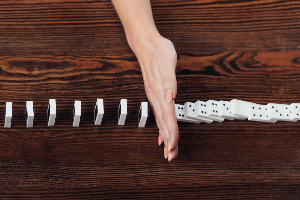 visão cortada da mulher impedindo dominós de cair na mesa de madeira
 - Foto, Imagem