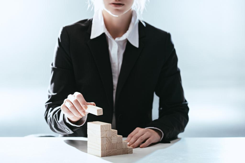 cropped view of woman putting wooden brick on top of wooden blocks symbolizing career ladder with backlit - Photo, Image