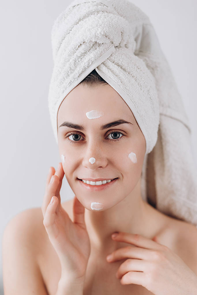 Młoda kobieta szczęśliwa opatrywana ręcznik stosowania kremu do twarzy, do pielęgnacji skóry. Koncepcja pielęgnacji skóry. Wspaniały kaukaski kobieta z doskonałym zdrowiu czystą skórę.  - Zdjęcie, obraz