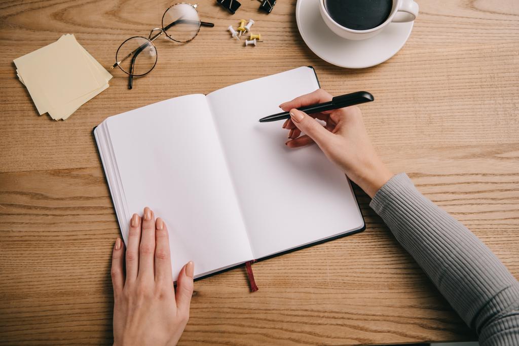 vue recadrée de femme d'affaires écrivant dans un cahier sur le lieu de travail avec des lunettes et une tasse de café
 - Photo, image