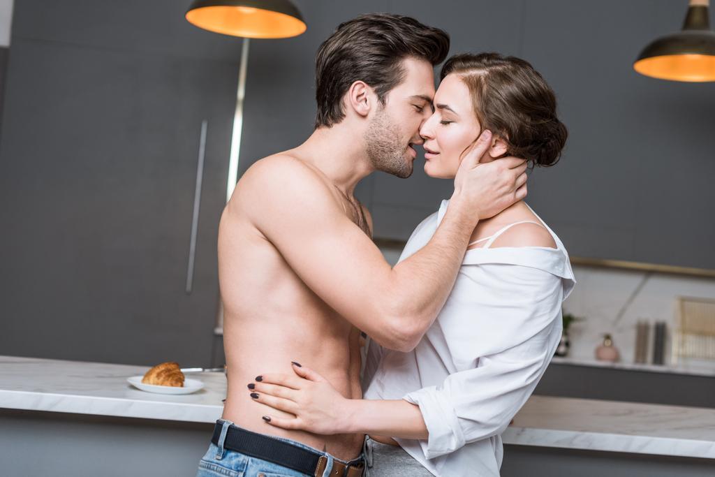 Erwachsenes Paar küsst sich in Küche mit geschlossenen Augen - Foto, Bild