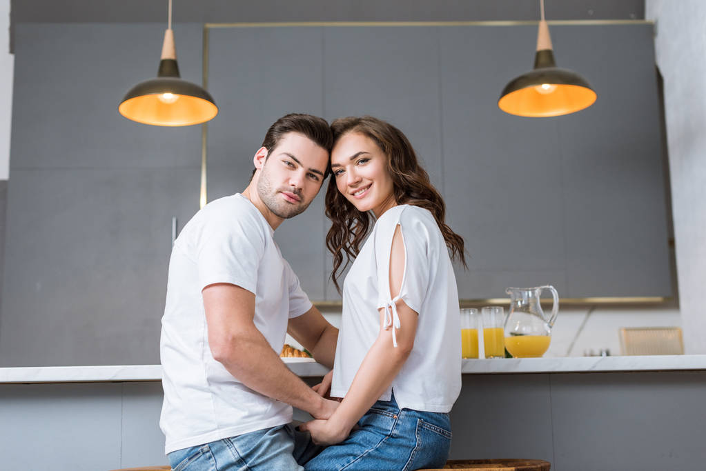 happy couple looking at camera and holding hands in kitchen  - Photo, Image
