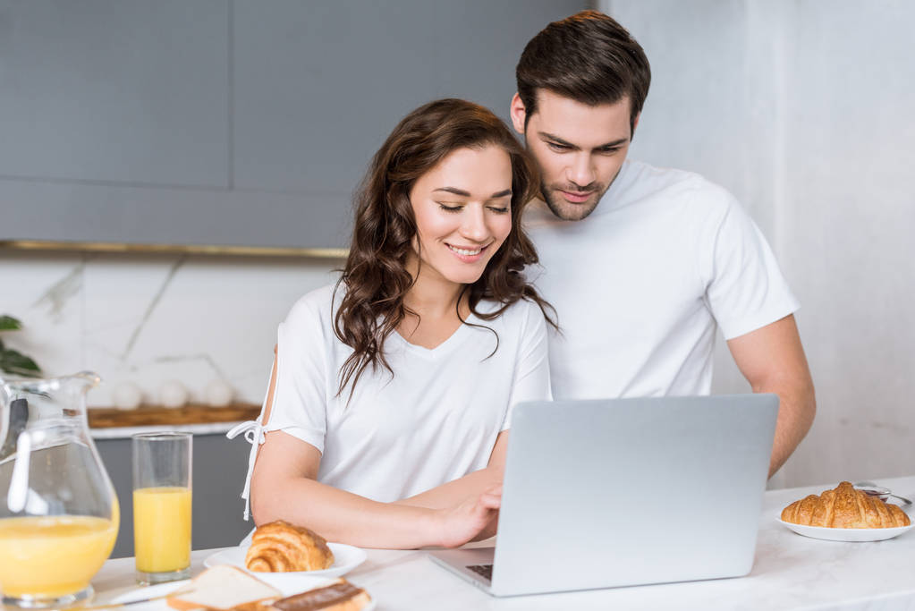 mujer feliz mirando portátil cerca novio guapo en la cocina
  - Foto, imagen