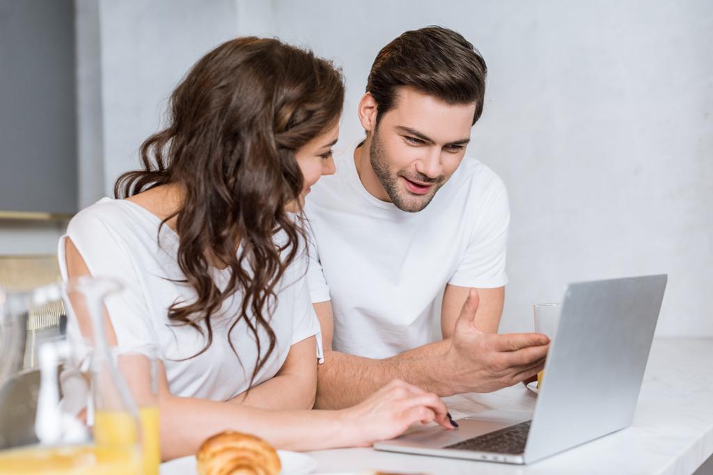 привлекательная женщина смотрит на парня с помощью ноутбука на кухне
  - Фото, изображение
