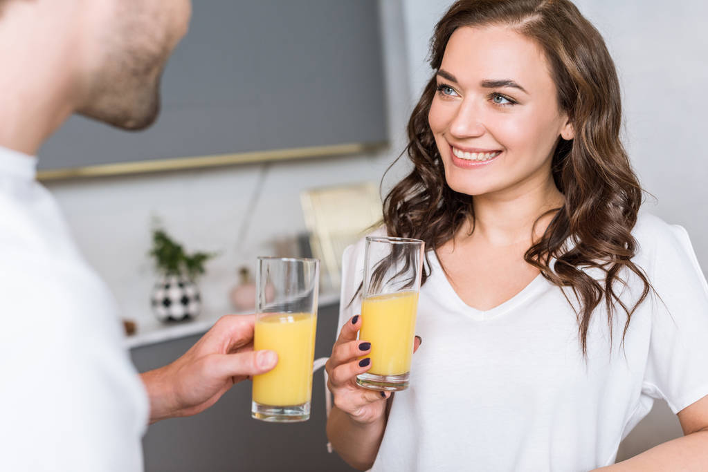 foco seletivo da mulher atraente sorrindo enquanto segura o vidro com suco de laranja perto do namorado
 - Foto, Imagem