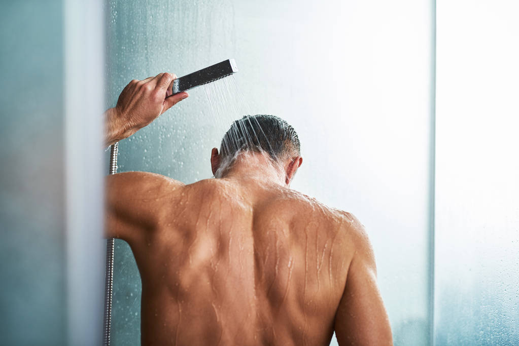 Νεαρός άνδρας χρησιμοποιώντας το κεφάλι ντους χειρός πλένοντας ο ίδιος στο μπάνιο - Φωτογραφία, εικόνα